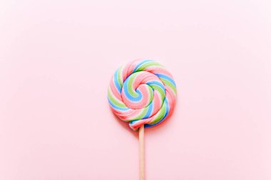 Çubukta renkli lolipop girdabı. Pembe arka planda çizgili sarmal renkli şeker, üst manzara