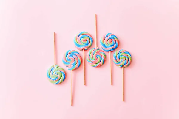Pirulitos coloridos rodopiam em paus. Listrado espiral de doces multicoloridos no fundo rosa, vista superior — Fotografia de Stock