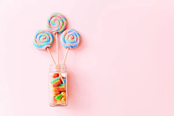 Bunte Lutscher wirbeln auf Stöcken in Glasflaschen. Gestreifte Spirale bunte Bonbons auf rosa Hintergrund, Ansicht von oben — Stockfoto