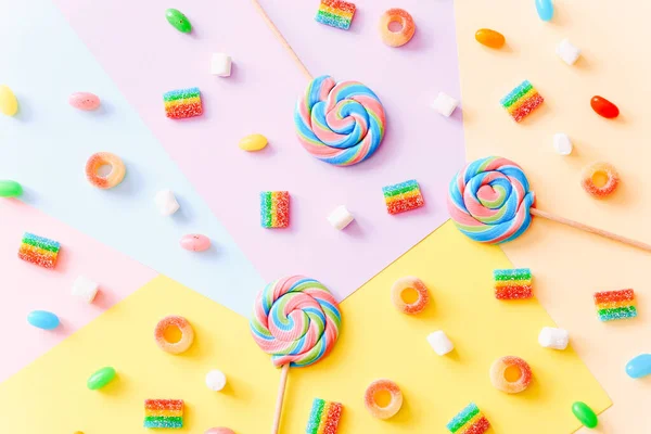 Färgglada klubbor virvlar på pinnar och gelé godis på färgglada bakgrund, ovanifrån — Stockfoto