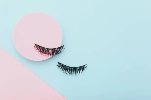 False eyelashes on colored blue and pink background, top view — Stock Photo, Image