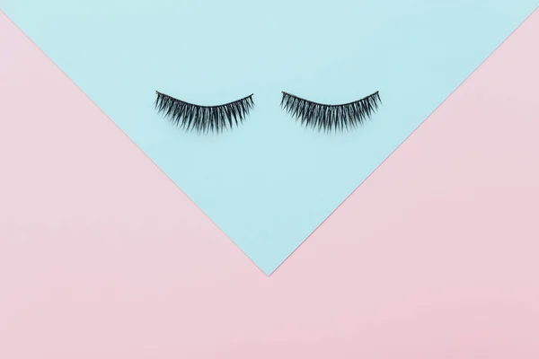 False eyelashes on colored blue and pink background, top view — Stock Photo, Image