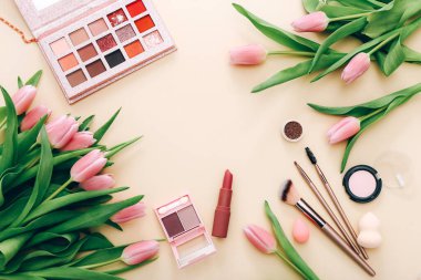 Makyaj için kozmetik ürünleri ve açık bej arka planda pembe laleler ile düz konum