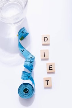 Bir bardak su ve beyaz zemin üzerinde kelime diyeti olan bir mezura.