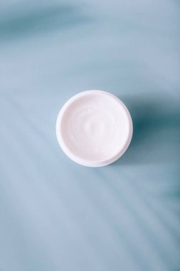 Mavi arka planda gölgeli kozmetik krem içeren beyaz bir kap aç. Kozmetik nemlendirici ürün.