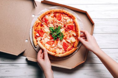Pizza kutusunda ve kadın eli beyaz ahşap arka planda pizza dilimleri alıyor.