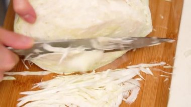 Mutfakta tahta kesme tahtasının üzerinde bıçaklı beyaz lahana ile kesilmiş kadın elleri.