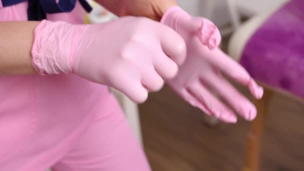 Профессиональная женщина косметолог надевает на руки голубые резиновые чистые стерильные перчатки перед выполнением процедуры по уходу за кожей лица клиентов. Концепция профессионализма в косметологии — стоковое видео