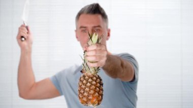 Bir adam ananası bir elinde bıçakla havada keser.