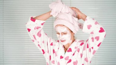 Komik, mutlu, çekici kadın yüzüne krem sür banyo aynasına bak, genç bayan başını havluyla sar.