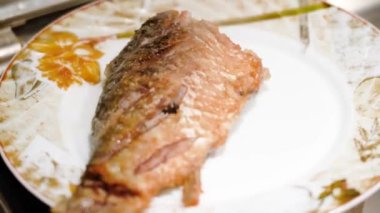 Adam tavaya sazan balığı koyuyor. Mutfak maşasıyla yakın plan erkek eli..