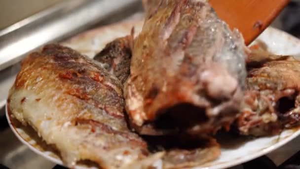 Człowiek kładzie karpie ryby na talerzu z patelni. Close-up męskie ręce z szczypcami kulinarnymi. — Wideo stockowe