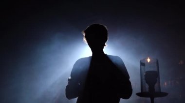 Portre adam geleneksel nargile piposu içiyor ve halka şeklinde duman bulutları yapıyor. Adam nargile kafeteryasında ya da bar barında duman üflüyor..