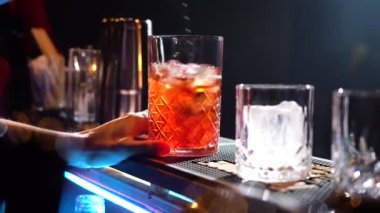 Barmen buz ekliyor ve kokteyl bardağında karıştırıyor. İçki barında kokteyl yapıyor.