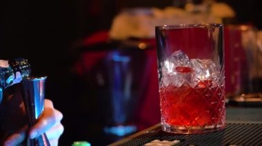 Barmen bar tezgahında kokteyl karıştırarak barmenlik kadehini dolduruyor. Yakın çekim.