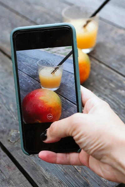 Kadın cep telefonuyla mango ve meyve suyu fotoğrafı çekiyor.