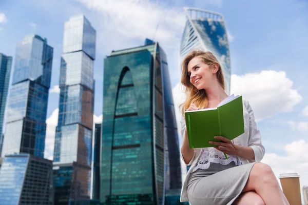 Молодая красивая женщина сидит aganst офисных зданий с зеленой тетради или дневника . — стоковое фото