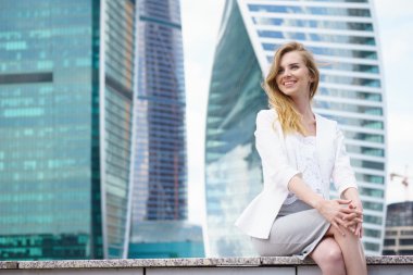 Şehir binaları önünde oturan genç kadın.