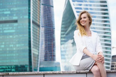 Şehir binaları önünde oturan genç kadın.