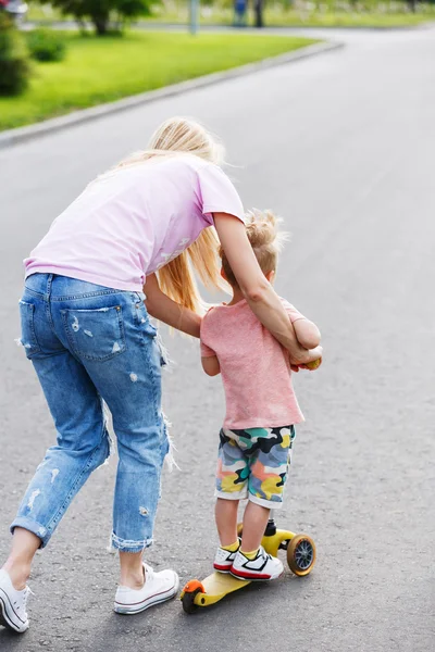 Beautiful girl teach his son to ride a scooter — Stock Photo, Image