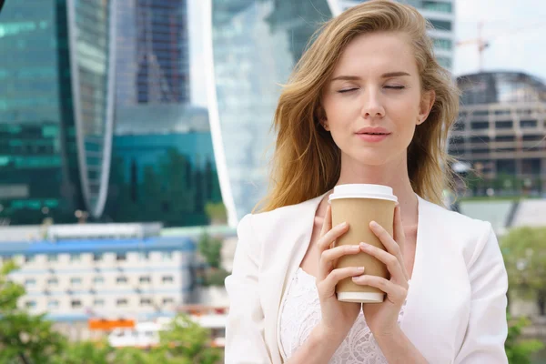 Geschäftsfrau Blondine hält Kaffee im Freien vor dem Hintergrund der Stadt — Stockfoto