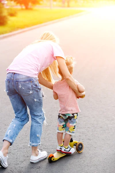 Bella ragazza insegnare a suo figlio a cavalcare uno scooter — Foto Stock