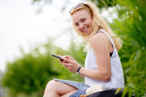 Hermosa joven sonriente con teléfono sentado — Foto de Stock