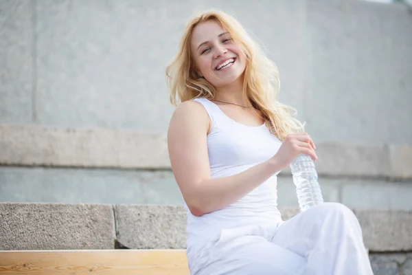 Девушка сидит со скрещенными ногами и держит бутылку с водой — стоковое фото