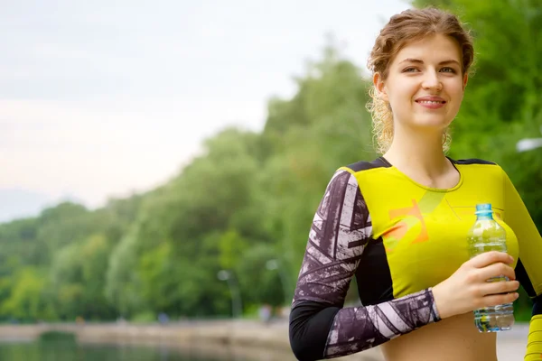 Женщина на улице в спортивном жёлтом костюме держит бутылку воды — стоковое фото