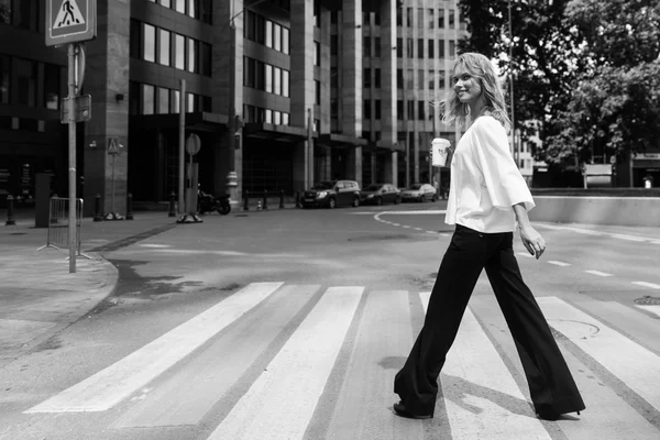 Stijlvolle vrouw het oversteken van de weg met koffie in moderne kwartaal — Stockfoto