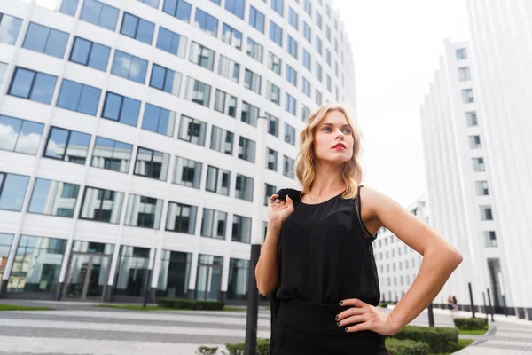 Blond kobieta w czarnej stojący w pobliżu białe budynki — Zdjęcie stockowe