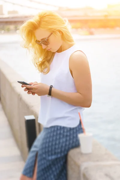 Mujer con cabello dorado mirando el teléfono inteligente al aire libre — Foto de Stock