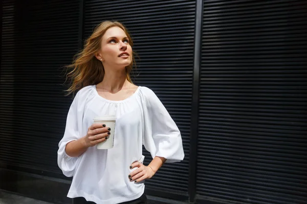 Woman with waving hair curiously looking up and holding coffee — Stock Photo, Image