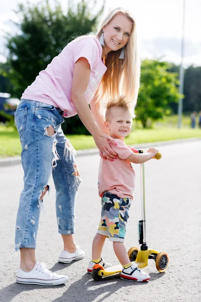 Bella ragazza insegnare a suo figlio a cavalcare uno scooter — Foto Stock