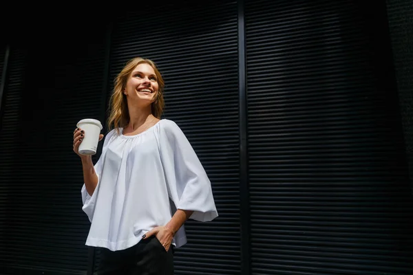 Lächelndes Mädchen mit Einweg-Kaffeetasse auf dunklem Wandhintergrund — Stockfoto