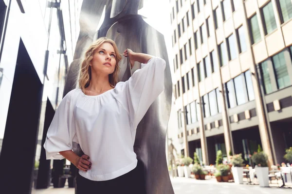 Atrakcyjny blond kobieta spogląda na tle nowoczesne rzeźby — Zdjęcie stockowe
