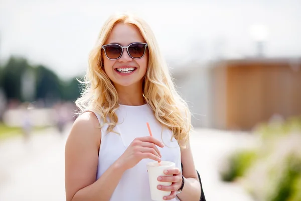 Молодая блондинка держит молочный коктейль с соломой и смотрит в камеру — стоковое фото