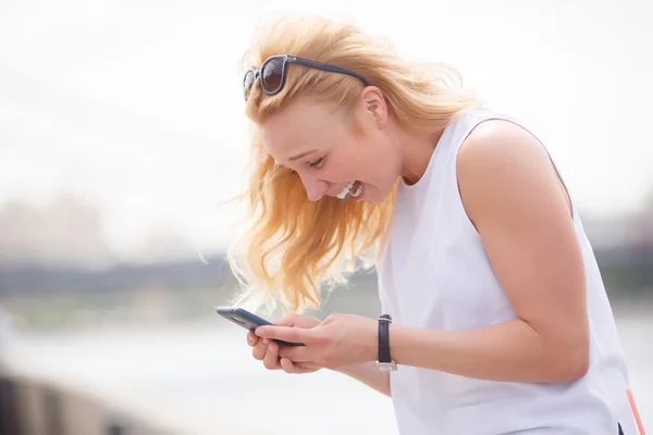 Linda chica rubia se ríe y mira en su teléfono — Foto de Stock