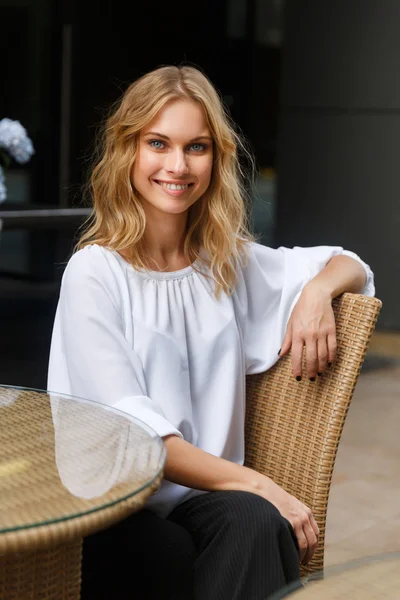 Молодая улыбающаяся блондинка, сидящая со скрещенными ногами за журнальным столиком — стоковое фото