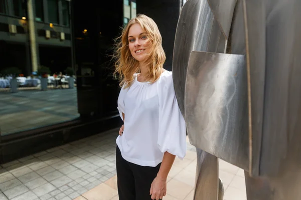 Lachende Kaukasische vrouw met krullend blond haar in de buurt van stalen sculptuur — Stockfoto