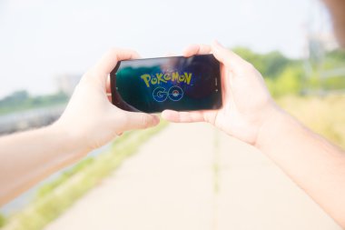 Adam onun perde Pokemon Go uygulaması ile gösterilen bir elinde telefon düzenlenen.