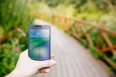 Adam onun perde Pokemon Go uygulaması ile gösterilen bir elinde telefon düzenlenen.