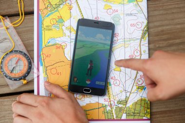 Maps, compas and hand show to phone screen with Pokemon Go application. clipart
