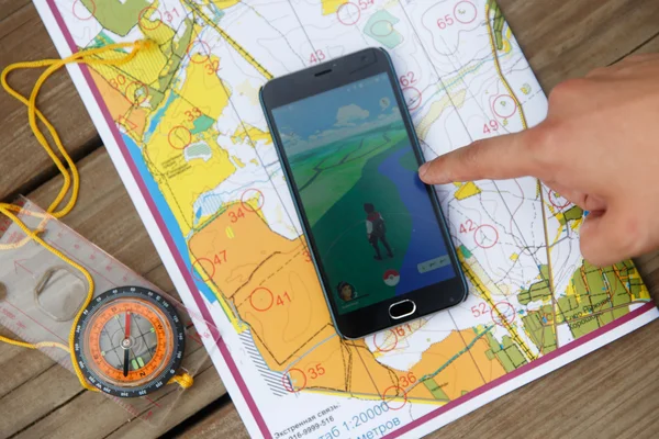 Mapas, compas y la mano muestran a la pantalla del teléfono con la aplicación Pokemon Go . — Foto de Stock