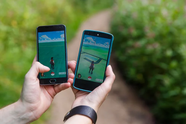 Dos amigos sostienen los teléfonos en las manos mostrando su pantalla con la aplicación Pokemon Go . — Foto de Stock
