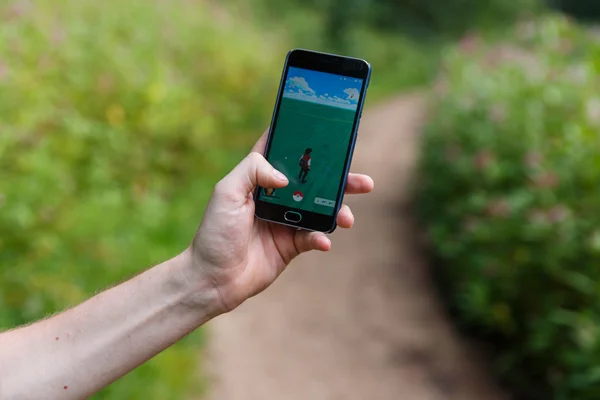 Hombre sostuvo el teléfono en una mano mostrando su pantalla con la aplicación Pokemon Go . — Foto de Stock