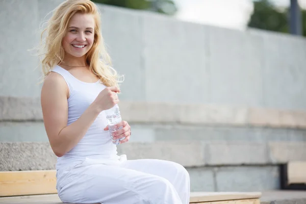 Блондинка в белом платье сидит на скамейке и отдыхает — стоковое фото