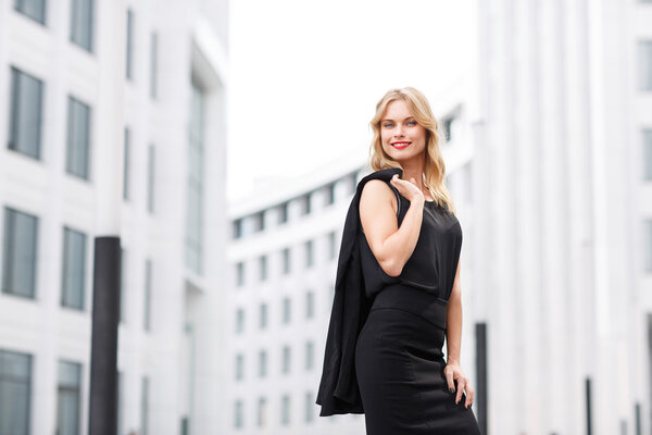 Блондинка в черной блузке и юбке, стоящая возле офиса
