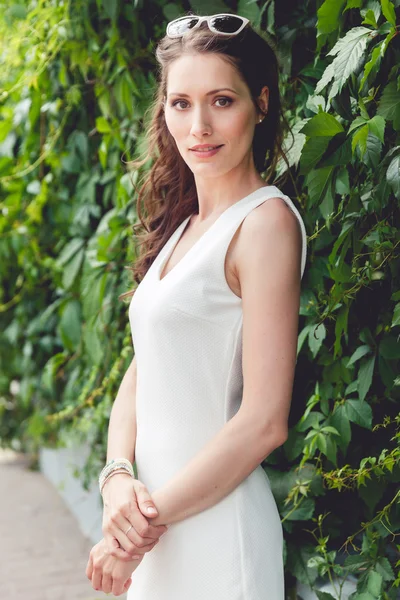 Hermosa mujer morena delgada en vestido blanco sobre fondo de follaje — Foto de Stock