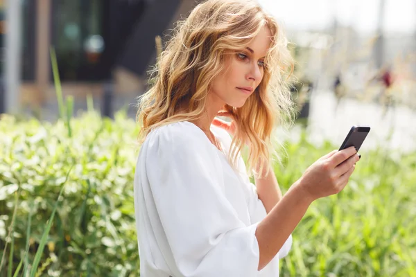 Chica joven con el pelo rubio rizado utilizando el teléfono inteligente al aire libre — Foto de Stock